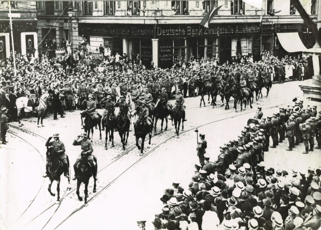 Historyczna defilada wojskowa na ulicy z tłumem widzów.