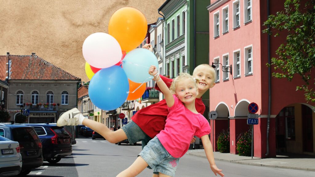 Dwoje dzieci skaczących z balonami na ulicy.