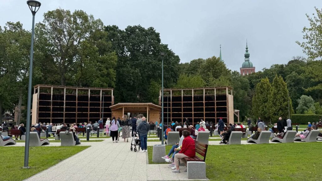 Tłum ludzi w parku przed drewnianą konstrukcją.