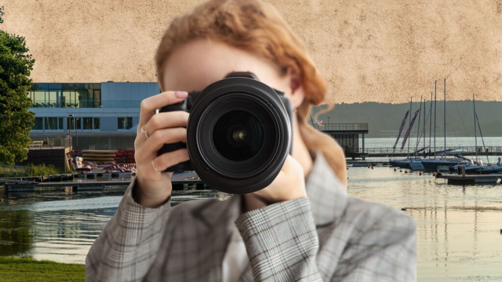 Osoba fotografująca aparatem, wklejona na tło widoku na jezioro Ukiel i przystań w Olsztynie.