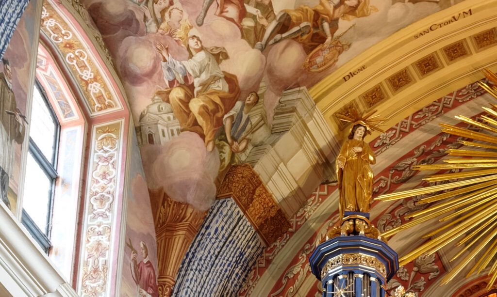 Fragment wnętrza kościoła z malowidłami i figurą świętej.