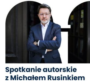 Mężczyzna w okularach stoi z założonymi rękami.