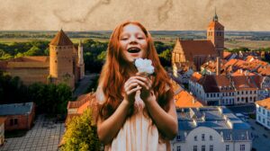 Uśmiechnięta dziewczynka z rudymi włosami trzyma kwiat na tle miasta.
