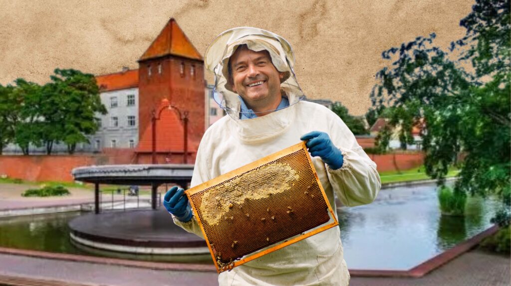 Mężczyzna w stroju pszczelarza z ramką miodu.