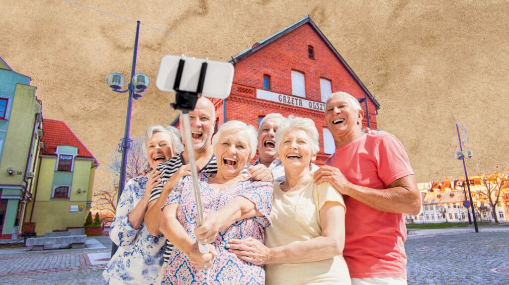Grupa uśmiechniętych seniorów robi selfie na tle budynku.