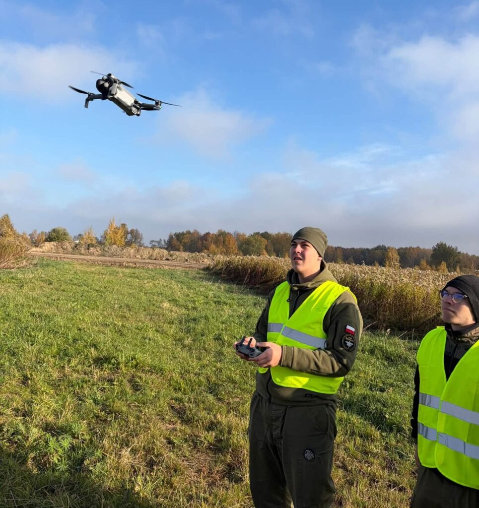 Mężczyźni w kamizelkach zdalnie sterują dronem w terenie.